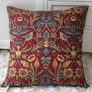May include: Red cushion with a floral pattern featuring birds, flowers, and leaves. The pattern is in shades of green, yellow, and blue.