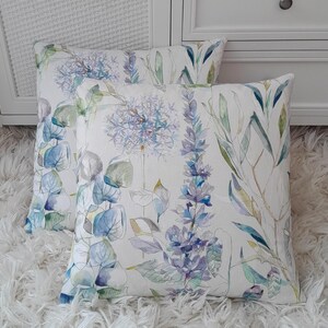 May include: Two decorative throw pillows with a floral pattern featuring watercolour-style blue, green, and purple flowers on a white background.