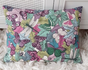 May include: A decorative pillow with a colorful butterfly and dragonfly pattern on a white background. The pillow is made of fabric and has a rectangular shape.