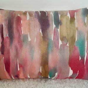 May include: A rectangular throw pillow featuring a vertical watercolor-style pattern with blended strokes of magenta, deep red, muted gold, teal, and soft purple against a white background, creating a multi-colored abstract design.