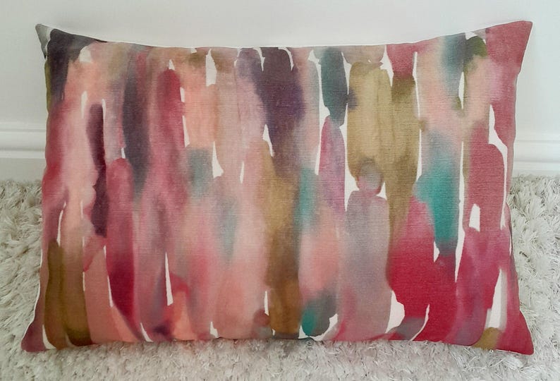 May include: A rectangular throw pillow featuring a vertical watercolor-style pattern with blended strokes of magenta, deep red, muted gold, teal, and soft purple against a white background, creating a multi-colored abstract design.