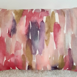 May include: A rectangular throw pillow featuring an abstract watercolor pattern with vertical brushstrokes in shades of magenta, muted olive green, soft purple, and dusty rose against a light off-white background with a visible fabric texture.