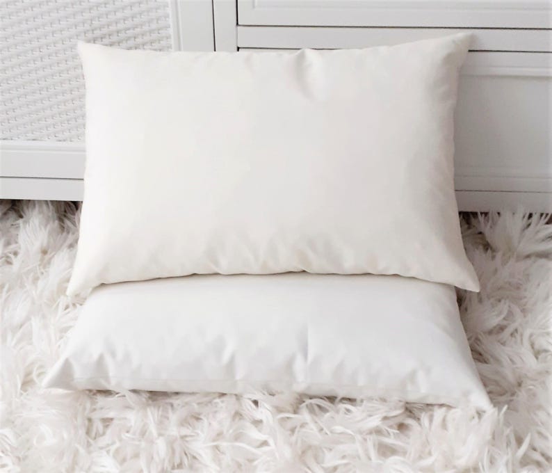 May include: Two white pillowcases stacked on top of each other on a white fluffy rug.