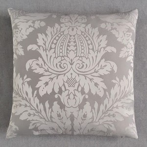 May include: A grey throw pillow with a white damask pattern. The pattern features a large, ornate floral design.