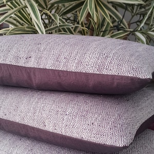 May include: Two purple and white patterned throw pillows with a dark purple border. The pillows are stacked on top of each other.