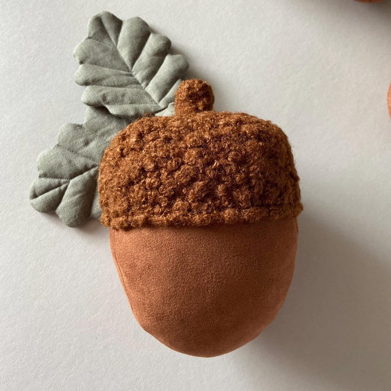 May include: A brown acorn-shaped plush toy with a crocheted top and a green felt leaf attached.