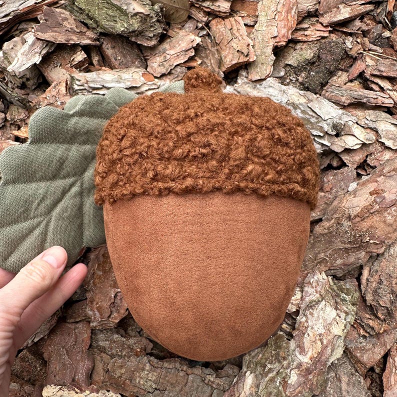 May include: A brown acorn-shaped plush toy with a fuzzy brown cap and a green felt leaf attached.