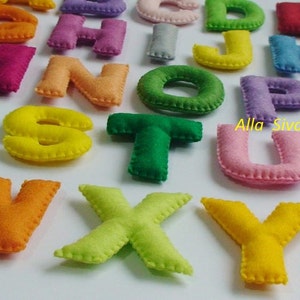 May include: A set of felt alphabet letters in various colors, including red, blue, green, yellow, orange, and purple. The letters are stitched with a white thread around the edges. The letters are arranged in alphabetical order.