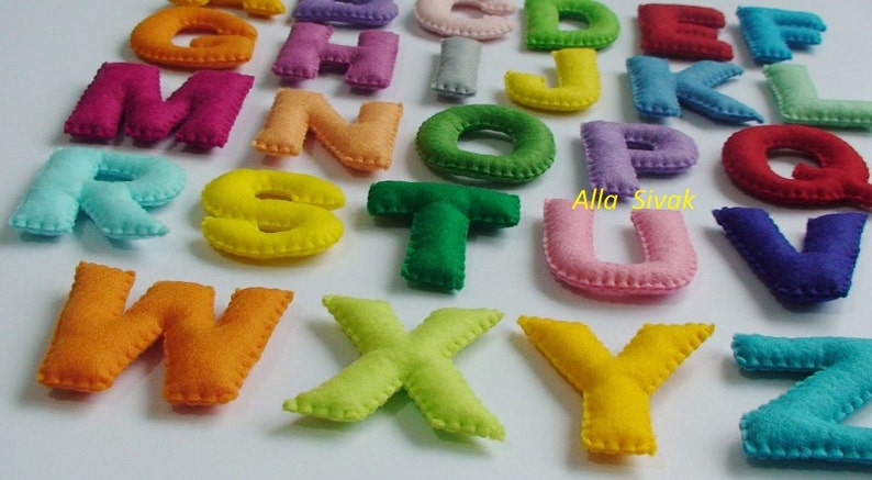 May include: A set of felt alphabet letters in various colors, including red, blue, green, yellow, orange, and purple. The letters are stitched with a white thread around the edges. The letters are arranged in alphabetical order.