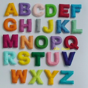 May include: A set of felt alphabet letters in various colors, including red, green, blue, yellow, orange, pink, and purple. The letters are arranged in alphabetical order and are sewn with a white thread.