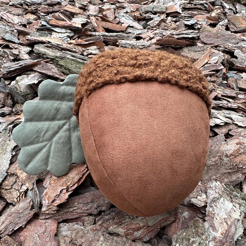 May include: A plush acorn toy with a brown felt body and a brown fuzzy top. The acorn has a green felt leaf attached to the side.