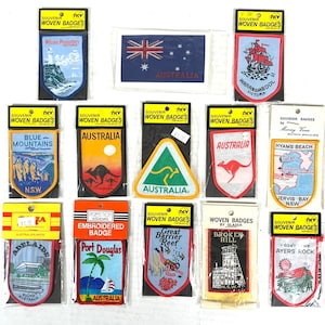 May include: A collection of souvenir woven badges featuring Australian landmarks and imagery. Badges include depictions of the Blue Mountains, Ayers Rock, the Great Barrier Reef, and more. Each badge is packaged with a cardboard header.