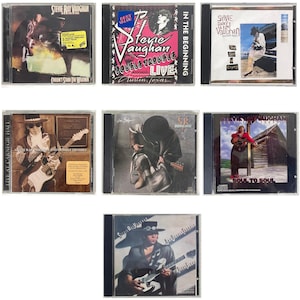 May include: Collection of Stevie Ray Vaughan CD albums. The album covers feature images of the musician playing guitar, with titles like "Couldn't Stand the Weather," "Soul to Soul," and "Live at Carnegie Hall." The CDs are in clear plastic cases.