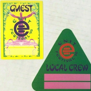 May include: Two Unity Festival 1996 passes. One is a yellow pass with the text "Guest" and a purple logo. The other is a green triangle pass with the text "Local Crew" and a pink blank space for a name.