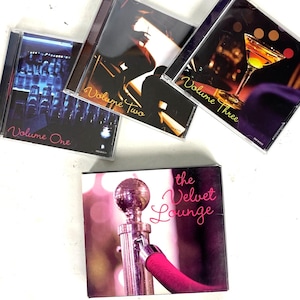 May include: A collection of four CD cases. Three cases are labeled "Volume One", "Volume Two", and "Volume Three". The fourth case is labeled "the Velvet Lounge". The cases have images of a bar, people, and a cocktail.