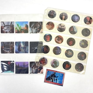 May include: A collection of Star Wars trading cards and stickers in a clear plastic binder. The binder has multiple rows of clear plastic pockets, each holding a different card or sticker. The cards and stickers feature various characters and scenes from the Star Wars movies.
