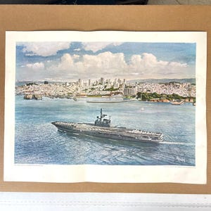 May include: Watercolor print of a naval aircraft carrier sailing on blue water, with a cityscape in the background. The sky is blue with white clouds. The print is on a white background.