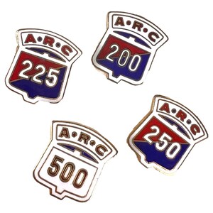 May include: Four shield-shaped metal enamel pins featuring the text A.R.C. at the top and the numbers 200, 225, 250, and 500 respectively. Each pin has a white border, a red upper section, and a blue lower section with silver-toned metal outlines.
