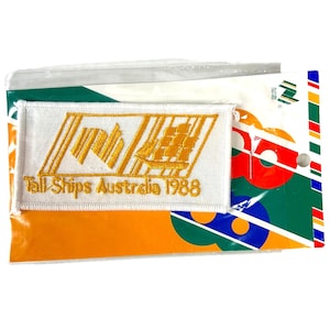 May include: A white rectangular patch with gold embroidery featuring a ship and the text "Tall Ships Australia 1988." The patch is packaged with a colorful backing that includes green, orange, red, and blue elements.