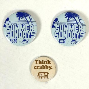 May include: Three round pinback buttons. Two blue buttons with a beach scene and the text "Summer Sundays". One beige button with the text "Think Crabby."