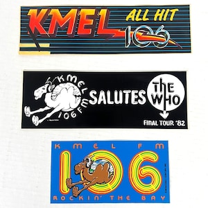 May include: Three vintage KMEL radio station bumper stickers. The top sticker has the text "KMEL ALL HIT 106" in red, orange, and yellow. The middle sticker is black with a white camel and the text "KMEL SALUTES THE WHO FINAL TOUR '82". The bottom sticker is blue with a camel and the text "KMEL 106 ROCKIN' THE BAY".