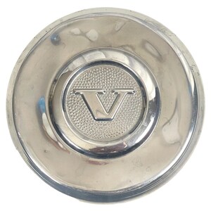 May include: A silver car hubcap with a raised, embossed "V" logo in the center.