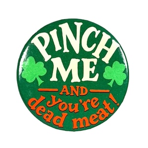 Puede incluir: Botón verde con texto blanco que dice "Pinch Me And You're Dead Meat!" con dos tréboles verdes a cada lado del texto.