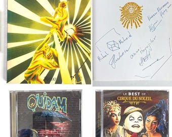 Può includere: Una collezione di tre articoli legati al Cirque du Soleil: un libro intitolato "Cirque du Soleil" con un'immagine colorata di artisti sulla copertina, un CD intitolato "Quidam" con un'immagine colorata di un artista che tiene un ombrello, e un CD intitolato "Le Best of Cirque du Soleil" con un'immagine colorata di tre artisti.