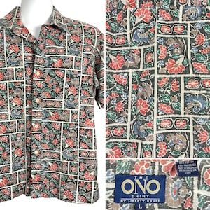 May include: A short-sleeved button-up shirt with a patterned design featuring a mix of red, green, blue, and brown colours. The shirt has a collar and a button closure. The label on the shirt reads "The Ono Shirt by Liberty House" and "L" for size.
