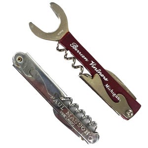 May include: Two vintage corkscrews. One is a burgundy and silver multi-tool with "Berrien Vintners Michigan" printed on the handle. The other is a silver corkscrew with "Paul Masson Vineyards" printed on the handle.
