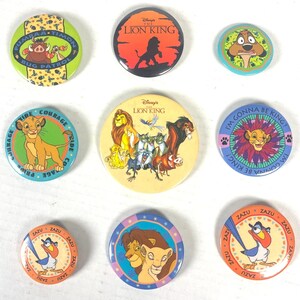 Puede incluir: Una colección de nueve botones redondos de personajes de El Rey León de Disney. Los botones presentan personajes como Simba, Timón, Pumba y Zazú. Los botones son de varios colores, incluyendo naranja, azul, amarillo y verde.