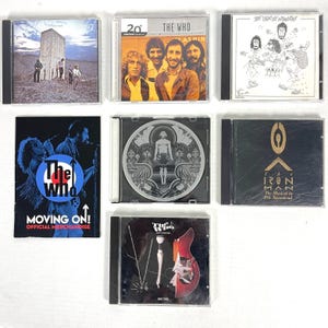 May include: A collection of nine compact discs featuring The Who, a rock band from England. The CDs are displayed on a shelf. The titles of the CDs include "The Who by Numbers", "The Iron Man", "The Who", "Moving On!" and "20th Century Masters - The Millennium Collection: The Who".