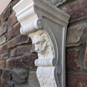 May include: White marble lion corbel with intricate details, measuring 13.5 inches in length. The corbel is mounted on a brick wall.