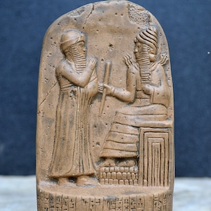May include: A brown stone replica of the Code of Hammurabi, a Babylonian law code from ancient Mesopotamia. The replica is 6.5 inches tall and features a relief sculpture of Hammurabi receiving the law from the sun god Shamash. The replica is inscribed with cuneiform script.