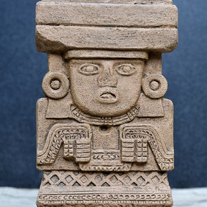 May include: A brown stone sculpture of a figure wearing a headdress and a patterned garment. The sculpture is 8 inches tall and is called "Chalchiuhtlicue Stele".