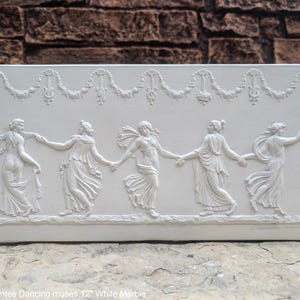 May include: White marble relief sculpture of five women dancing in a circle. The women are wearing flowing robes and have wreaths in their hair. The sculpture is 12 inches wide and is titled "Bacchantes Dancing Muses".