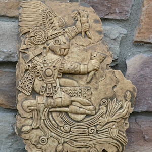May include: A beige stone relief sculpture of a figure wearing a headdress and holding a staff. The sculpture is carved with intricate details and is mounted on a wall. "Aztec Codex Chalchiuhtlicue 11" Aged Stone" is written below the sculpture.