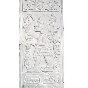 May include: White plaster relief sculpture of a Mayan figure with a headdress and a staff. The figure is standing on a platform with glyphs and other symbols. The sculpture is in a rectangular shape.