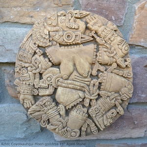 May include: A circular stone relief sculpture depicting the Aztec Moon goddess Coyolxauhqui. The sculpture is 11 inches in diameter and features intricate carvings of the goddess's body, face, and headdress. The stone is aged and has a light brown color.