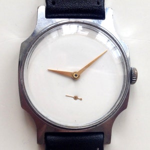 Puede incluir: Un reloj de pulsera plateado con una esfera blanca y agujas doradas. El reloj tiene una correa de cuero negra.