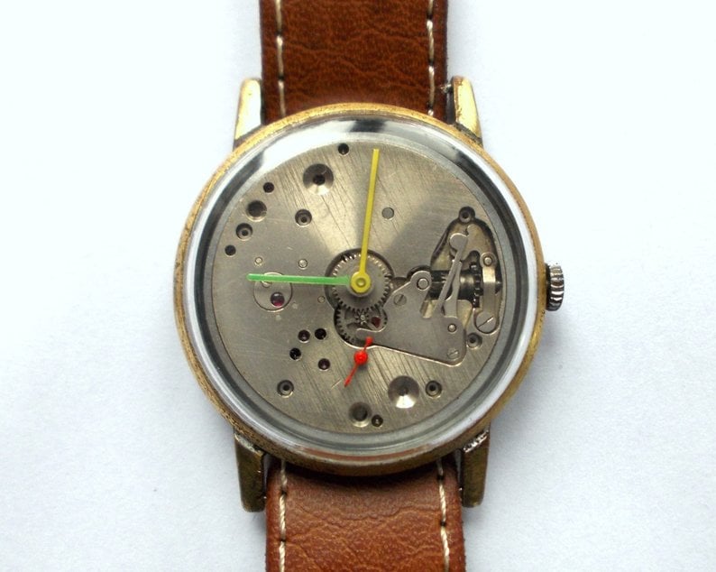 May include: A gold-tone wristwatch with a brown leather band. The watch face is open, revealing the inner workings of the watch.