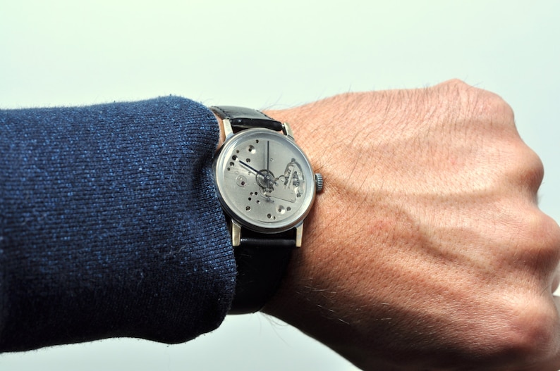 May include: A silver wristwatch with a skeletonized dial and black leather band. The watch is worn on a person's wrist.