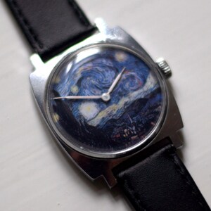 May include: A silver wristwatch with a black leather band. The watch face features a reproduction of Vincent van Gogh's "The Starry Night" painting.