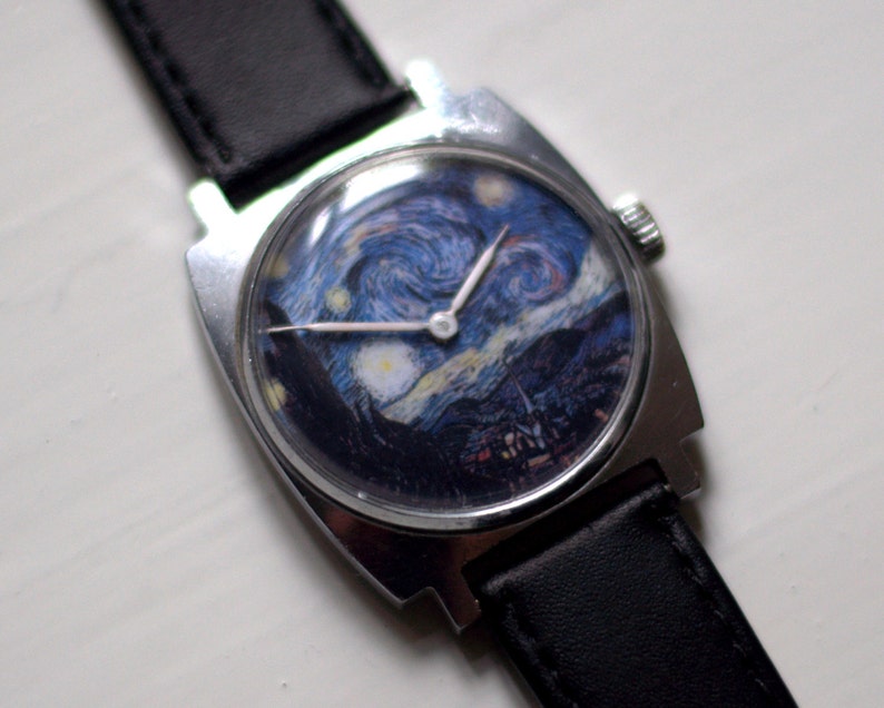 May include: A silver wristwatch with a black leather band. The watch face features a reproduction of Vincent van Gogh's "The Starry Night" painting.