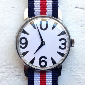 May include: A white wristwatch with black numbers and hands on a white face. The watch has a silver case and a red, white, and blue striped band.