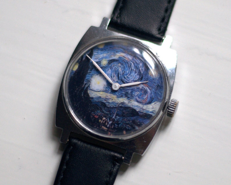 May include: A silver wristwatch with a black leather band. The watch face features a reproduction of Vincent van Gogh's "Starry Night" painting.
