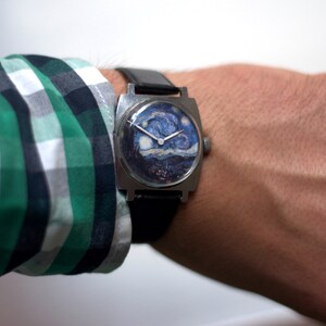 May include: A square-shaped wristwatch with a black leather band. The watch face features a printed image of Vincent van Gogh's "Starry Night" painting.