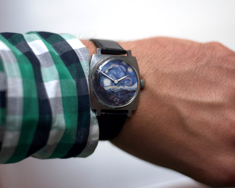 May include: A square-shaped wristwatch with a black leather band. The watch face features a printed image of Vincent van Gogh's "Starry Night" painting.