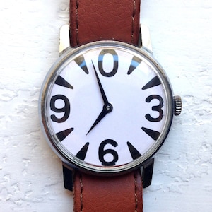May include: A silver wristwatch with a white face and black numbers. The watch has a brown leather band.