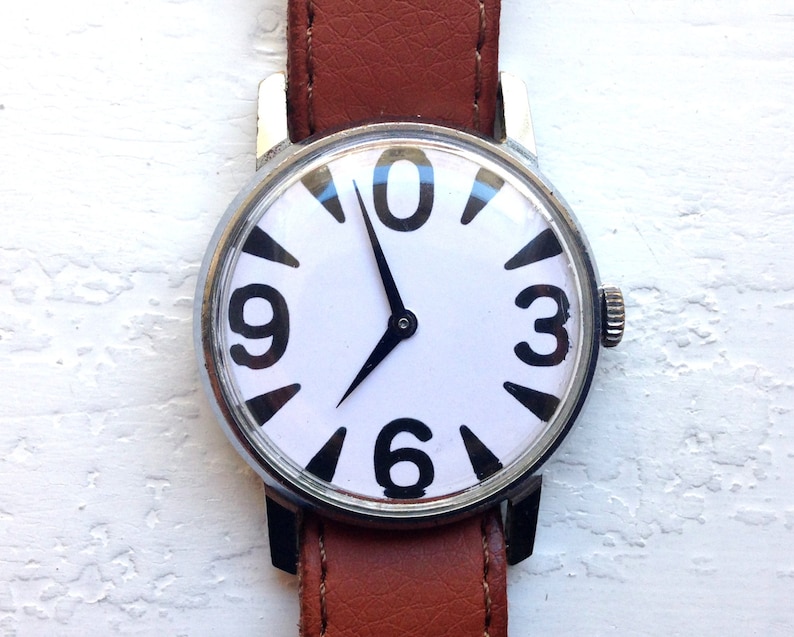 May include: A silver wristwatch with a white face and black numbers. The watch has a brown leather band.